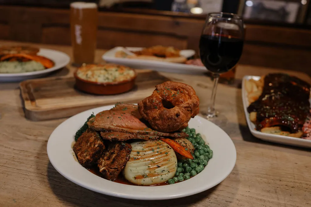 Two Sunday roasts with Yorkshire puddings, mash and greens, set out with a glass of red